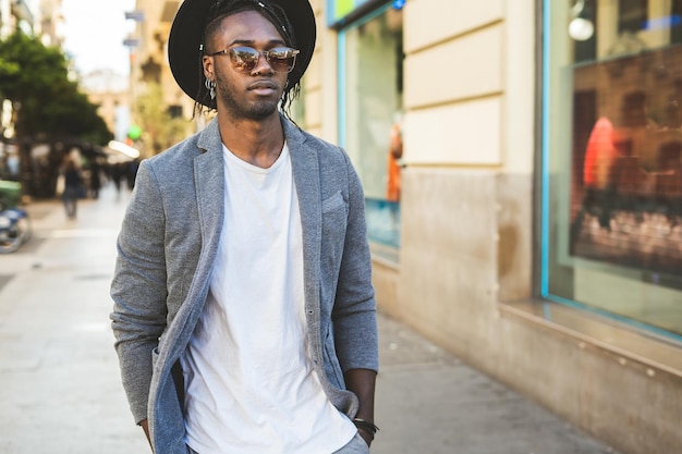 Un jeune homme à la mode avec un chapeau se tient dans la ville.