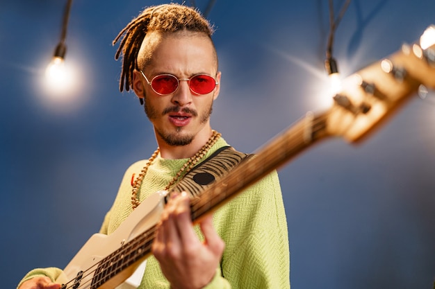 Jeune homme à la mode dans des lunettes de soleil roses jouant de la guitare avec joie