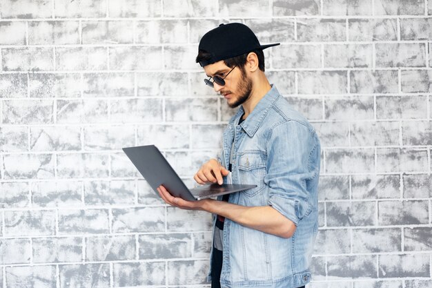 Jeune homme moderne avec ordinateur portable en mains sur le mur de mur de briques.