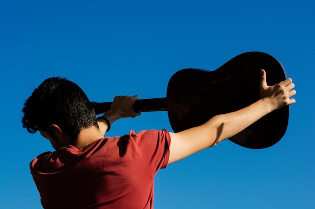 Jeune homme montant une guitare acoustique dans le ciel