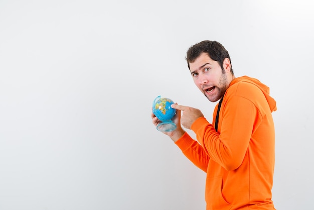 Jeune homme montrant le globe avec son doigt dans l'étonnement sur fond blanc