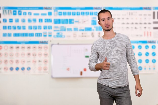 Jeune homme montrant des pouces vers le haut sur l'arrière-plan des affiches de formation floues avec des panneaux de signalisation