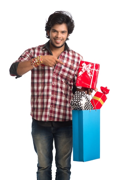 Jeune homme montrant rakhi sur sa main avec des sacs à provisions et une boîte-cadeau à l'occasion du festival Raksha Bandhan.