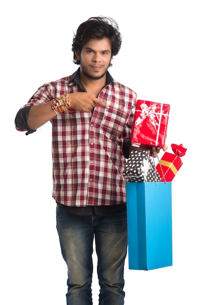 Jeune homme montrant rakhi sur sa main avec des sacs à provisions et une boîte-cadeau à l'occasion du festival Raksha Bandhan.