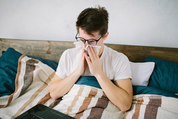 Jeune homme avec mouchoir. Un malade sur le lit a le nez qui coule. l'homme fabrique un remède contre le rhume.