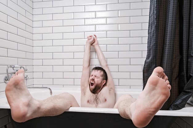 Un jeune homme mouillé se détend dans un bain en fonte avec des jambes qui bâillent et s'étirent