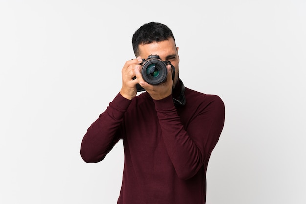 Jeune homme sur un mur blanc isolé avec une caméra professionnelle