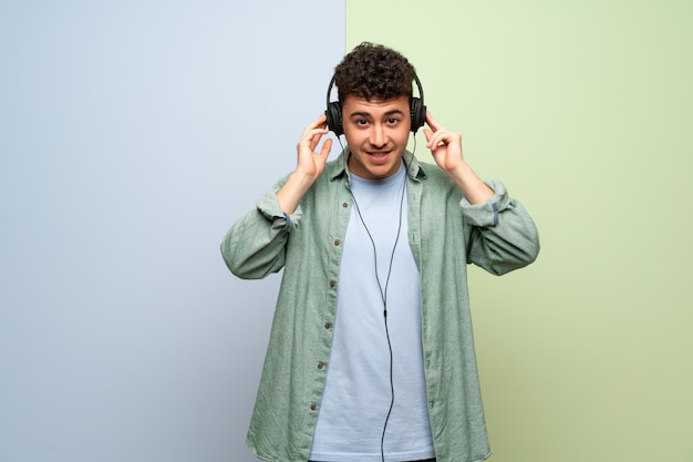 Jeune homme sur un mur bleu et vert, écouter de la musique avec des écouteurs