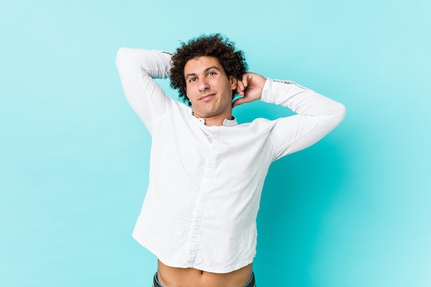 Jeune homme mûr bouclé portant une élégante chemise qui s'étend des bras, position détendue.