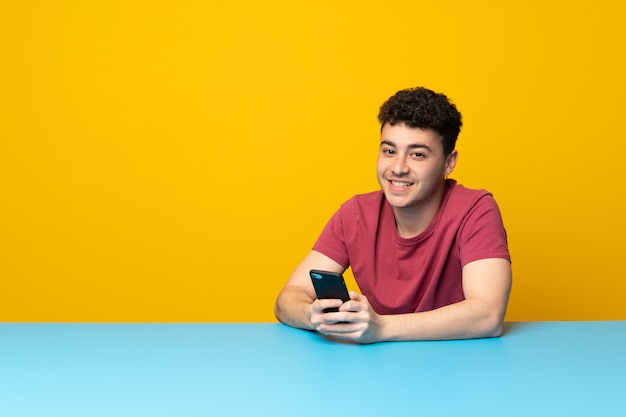 Jeune homme avec mur coloré et table envoyant un message avec le téléphone portable