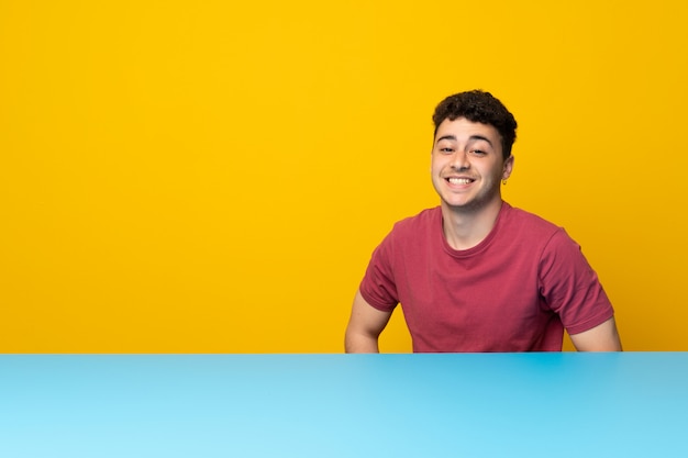 Jeune homme avec mur coloré et table en riant