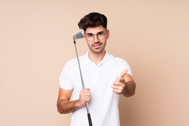 Jeune homme sur mur isolé jouant au golf et pointant vers l'avant