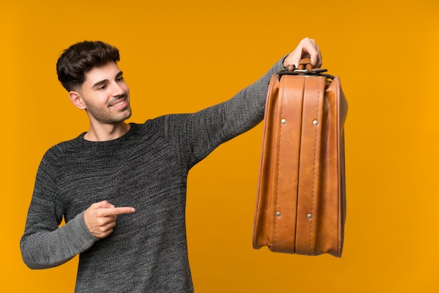 Jeune homme sur mur isolé tenant une mallette vintage