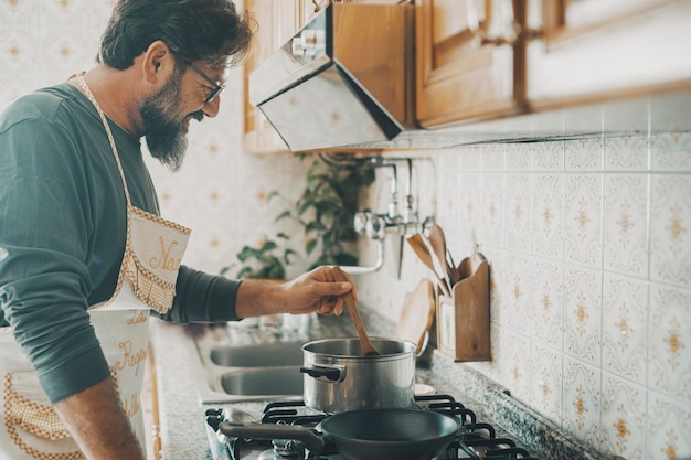 Un jeune homme mûr à la maison cuisinant seul en souriant et en s'amusant Activité de loisirs de la vie domestique à l'intérieur Les hommes de 50 ans cuisinent et profitent d'un style de vie unique Mari travaillant dans la cuisine