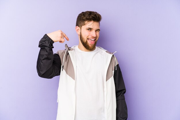 Jeune homme sur mur violet personne pointant à la main vers un espace vide de chemise, fier et confiant