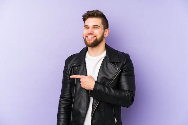 Jeune homme sur le mur violet, souriant et pointant de côté, montrant quelque chose à l'espace vide.