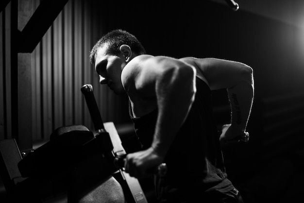 Jeune homme musclé avec un beau corps parfait portant des vêtements de sport faisant des pompes sur les barres pendant l'entraînement sportif dans une salle de sport moderne, couleur noir et blanc. Concept de mode de vie sain.