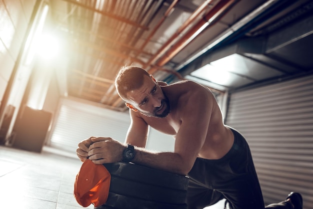 Jeune homme musclé d'épuisement se reposant après un entraînement croisé intensif au gymnase du garage.