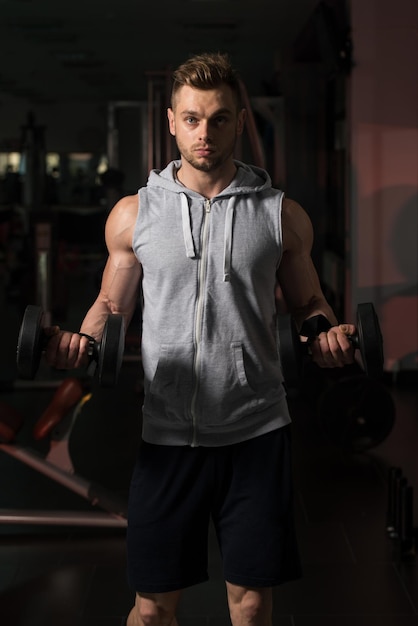 Jeune homme musclé faisant de l'exercice de poids lourd pour les biceps avec des haltères dans la salle de sport moderne du centre de remise en forme