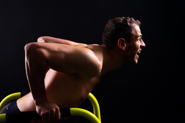 Un jeune homme musclé faisant des exercices de barre parallèles dans un studio rouge blanc foncé avec un espace de copie