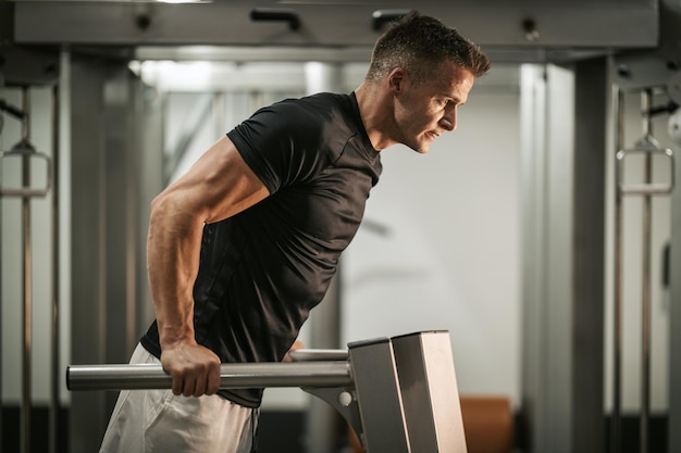 Jeune homme musclé faisant des exercices difficiles sur la machine lors d'un entraînement de musculation à la salle de sport.