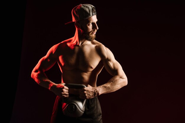 Jeune homme musclé faisant des exercices avec poids sur fond de studio noir.