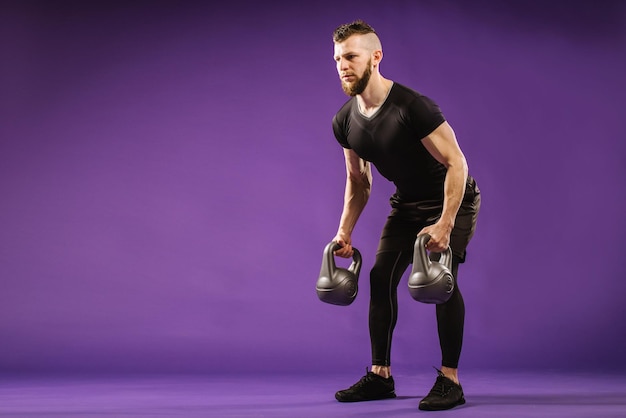 Jeune homme musclé faisant des exercices avec poids sur fond de studio violet. Copier l'espace