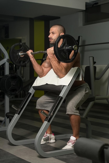 Jeune homme musclé faisant des exercices de poids lourds pour les biceps dans la salle de gym