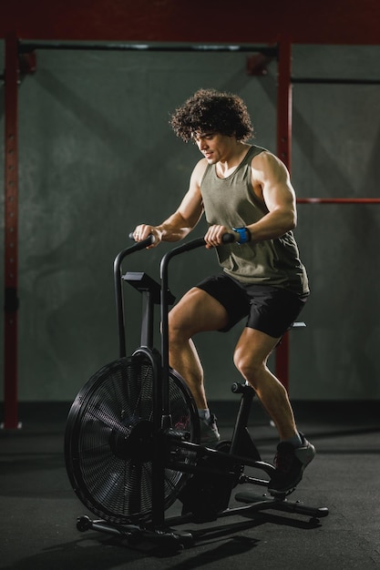 Un jeune homme musclé fait de l'entraînement crossfit à vélo dur dans la salle de gym.