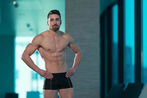 Jeune homme musclé Flexing Muscles au bord de la piscine et des chaises longues