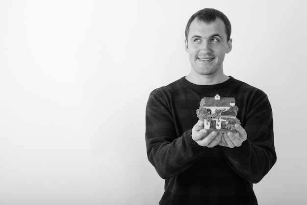 jeune homme musclé heureux souriant et pensant tout en tenant la figurine de la maison.