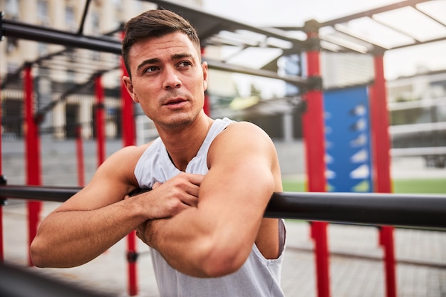 Un jeune homme musclé se repose sur des barres inégales après une séance d'entraînement en plein air en ville