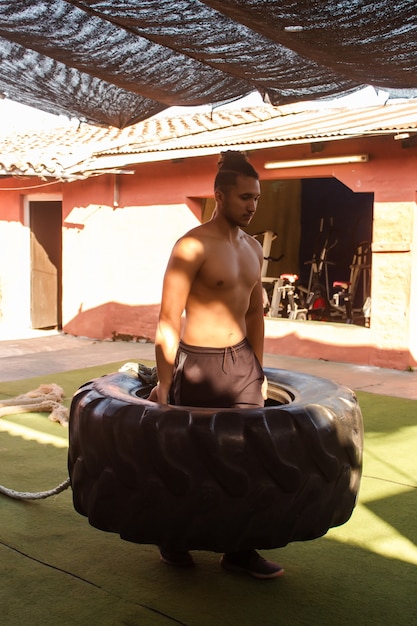 Jeune homme musclé soulevant un pneu de camion dans la cour du gymnase.