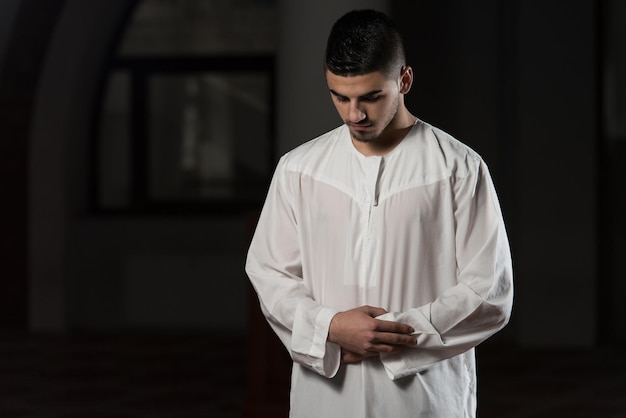 Jeune homme musulman faisant la prière traditionnelle à Dieu tout en portant une casquette traditionnelle Dishdasha