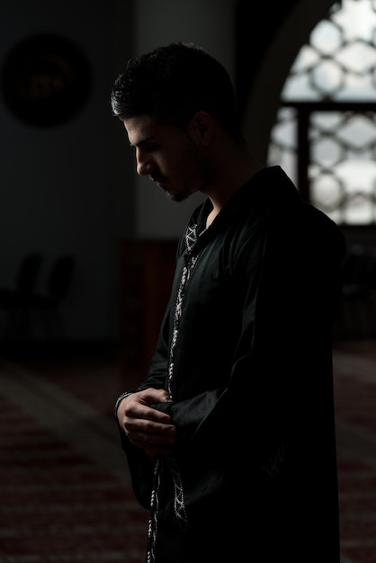 Jeune homme musulman faisant la prière traditionnelle à Dieu tout en portant une casquette traditionnelle Dishdasha