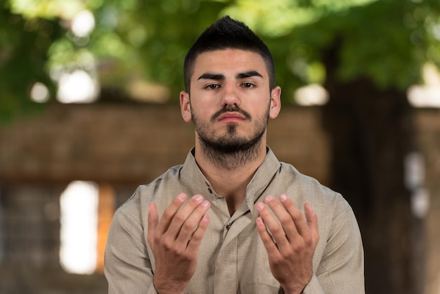 Jeune homme musulman faisant la prière traditionnelle à Dieu tout en portant une casquette traditionnelle Dishdasha