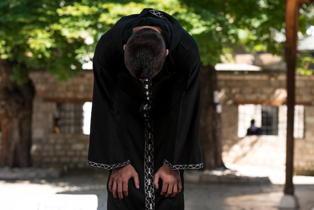 Jeune homme musulman faisant la prière traditionnelle à Dieu tout en portant une casquette traditionnelle Dishdasha