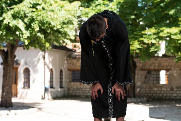 Jeune homme musulman faisant la prière traditionnelle à Dieu tout en portant une casquette traditionnelle Dishdasha