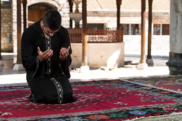 Jeune homme musulman faisant la prière traditionnelle à Dieu tout en portant une casquette traditionnelle Dishdasha