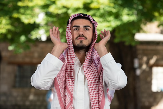 Jeune homme musulman faisant la prière traditionnelle à Dieu tout en portant une casquette traditionnelle Dishdasha