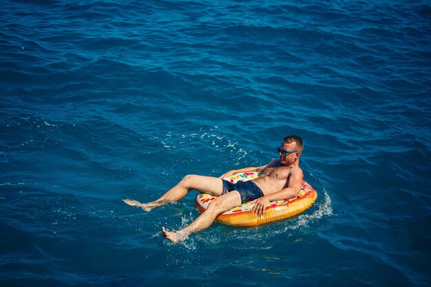 Un jeune homme nage en pleine mer sur un anneau gonflable par une journée ensoleillée Tourisme de vacances d'été en vacances