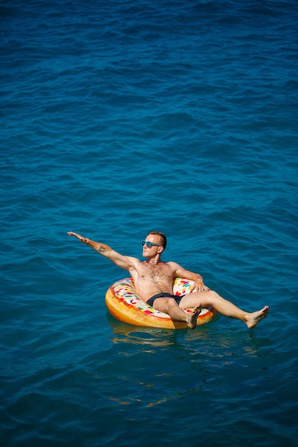 Un jeune homme nage en pleine mer sur un anneau gonflable par une journée ensoleillée. Vacances d'été, touriste en vacances