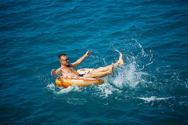 Un jeune homme nage en pleine mer sur un anneau gonflable par une journée ensoleillée. Vacances d'été, touriste en vacances