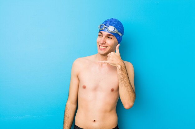 Jeune homme nageur montrant un geste d'appel de téléphone portable avec les doigts.