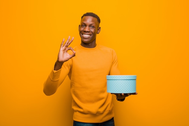 Photo jeune homme noir afro-américain contre le mur orange avec un cadeau