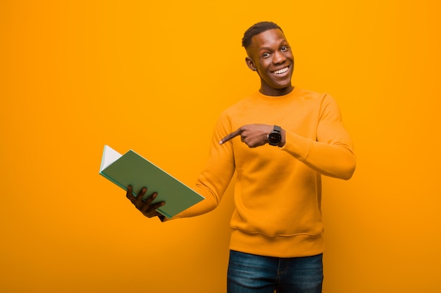 Jeune homme noir afro-américain contre le mur orange avec un livre