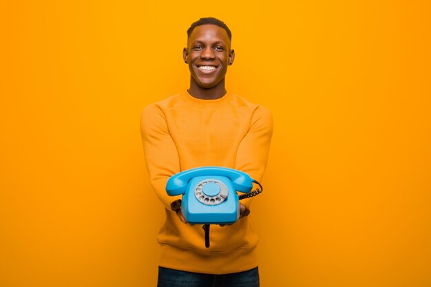 Jeune homme noir afro-américain contre le mur orange avec un téléphone vintage