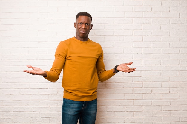 Jeune homme noir afro-américain à la perplexité, confus et stressé, se demandant entre les différentes options, se sentant incertain contre le mur de briques