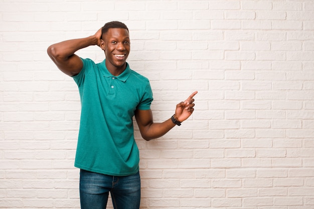 Jeune homme noir afro-américain en riant, l'air heureux, positif et surpris, réalisant une excellente idée pointant vers l'espace de copie latérale sur le mur de briques