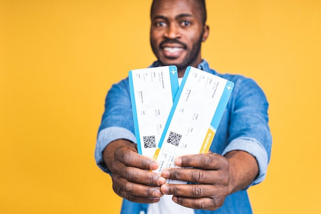 Jeune homme noir afro-américain souriant heureux tenant des billets d'embarquement isolés sur fond jaune.